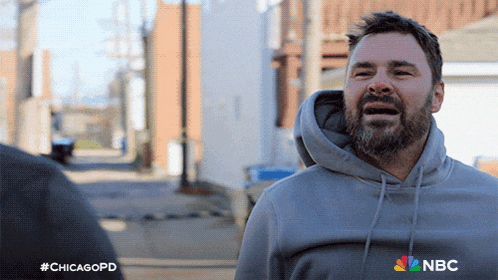 a man with a beard wearing a grey hoodie with nbc on the bottom