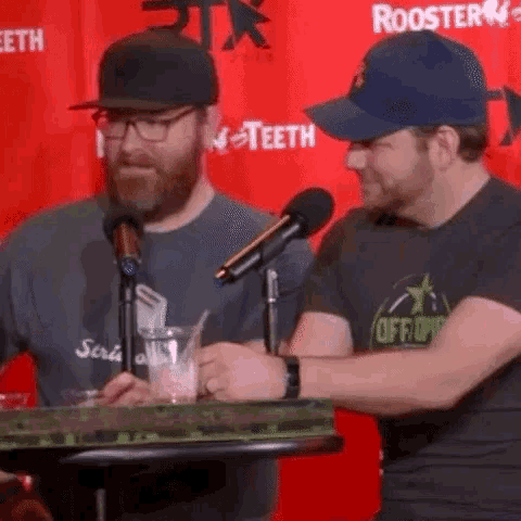 two men are speaking into microphones in front of a red backdrop that says rooster teeth