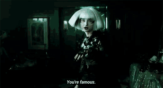 a woman in a white wig and gloves is standing in a dark room .