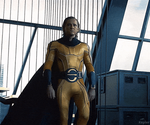 a man in a yellow superhero costume is standing in front of a window with kepler written on the bottom right