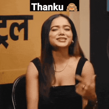 a woman in a black top is sitting in front of a yellow sign that says thanku .