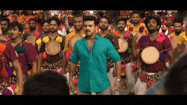 a man in a green shirt is standing in front of a large group of men playing drums .