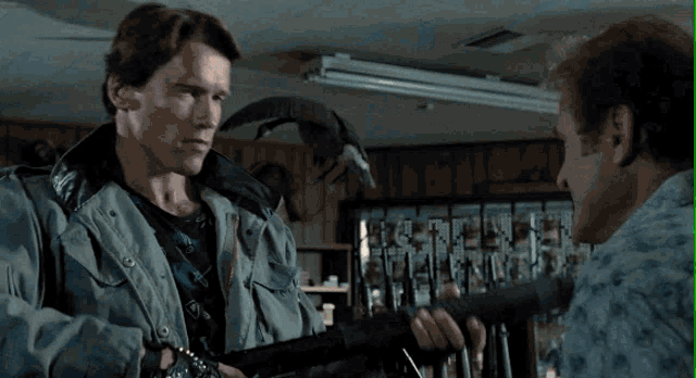a man is holding a gun in front of a wall of guns with tags on them