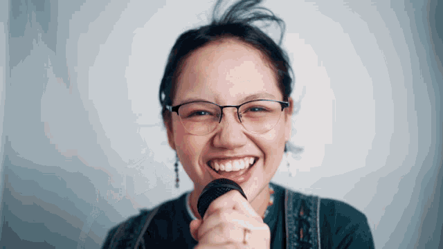 a woman with glasses is singing into a microphone and smiling