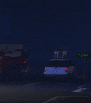 a blurred image of a car driving down a street at night with a fire truck in the background