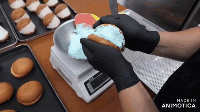 a person wearing black gloves is putting blue frosting on a donut on a scale that says cas