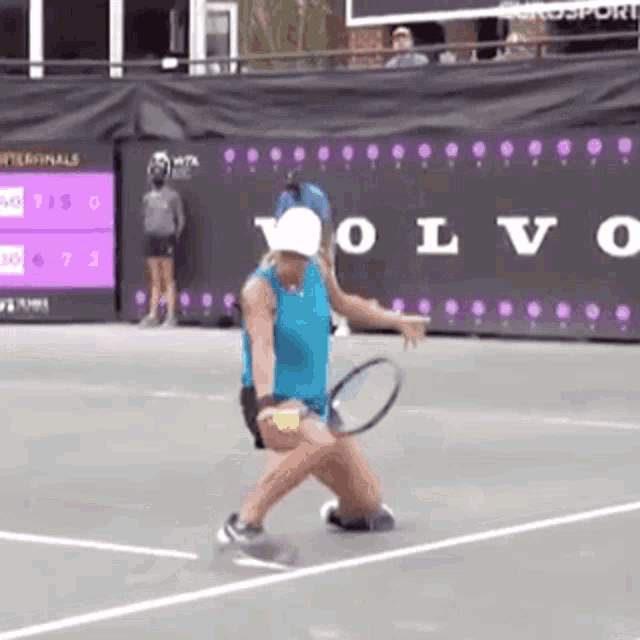 a woman is playing tennis on a tennis court in front of a volvo sign .
