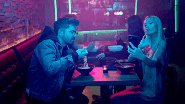 a group of people are sitting at a table in a restaurant eating noodles and taking a selfie