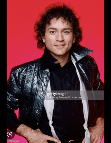 a man wearing a black leather jacket and a black shirt is standing in front of a pink background .
