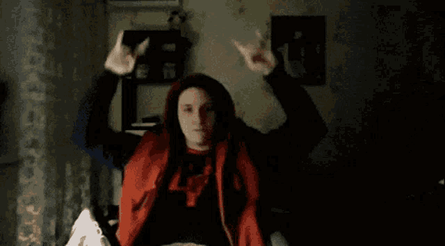 a man wearing a red vest with the letter l on it is sitting in a dark room with his arms outstretched .