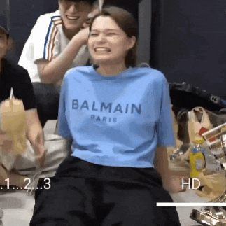 a woman wearing a blue balmain paris t-shirt is laughing