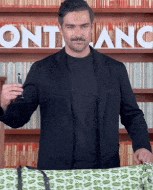 a man in a black suit holds a pen in front of a montblanc sign