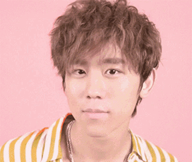 a young man with curly hair is wearing a yellow and white striped shirt and a necklace .
