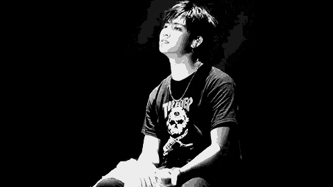 a black and white photo of a young man wearing a t-shirt with a skull on it and a necklace .