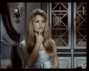 a woman in a white dress holds her finger to her lips in a room