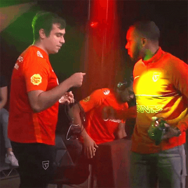 a man wearing an orange shirt that says vodafone talks to another man