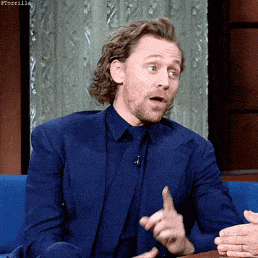 a man in a blue suit and tie is sitting on a blue couch