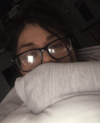 a person wearing glasses covering their face with a sweatshirt
