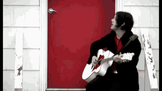 a man is playing a white guitar in front of a red door