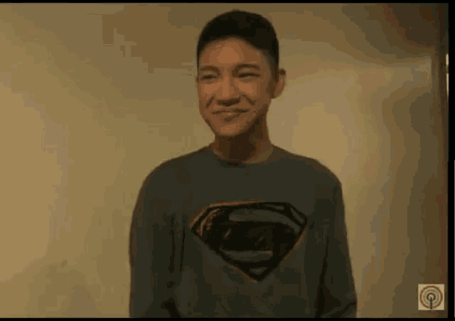 a young man wearing a gray superman sweatshirt is smiling .