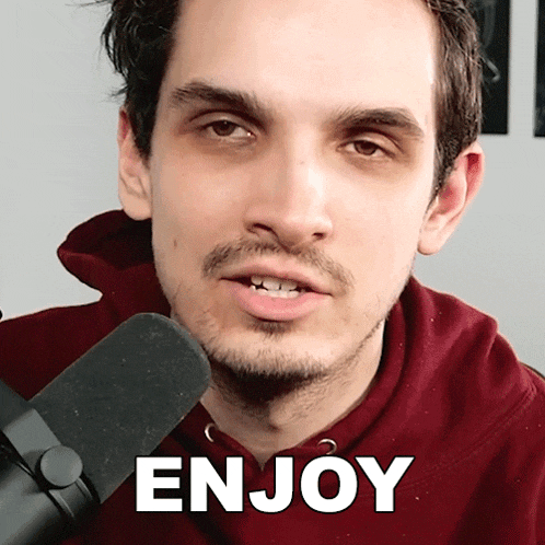 a man in a red hoodie stands in front of a microphone with the word enjoy written in white