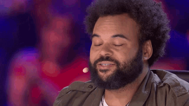 a man with a beard is sitting in front of a microphone and making a funny face .