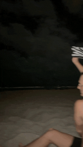 a shirtless man sitting on the beach holding a zebra print towel over his head