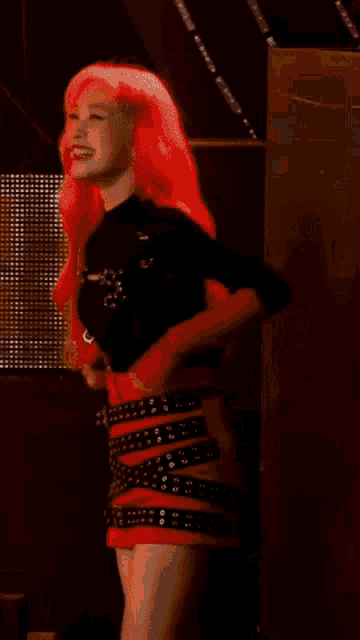 a woman with red hair is standing on a stage wearing a red skirt and a black shirt .