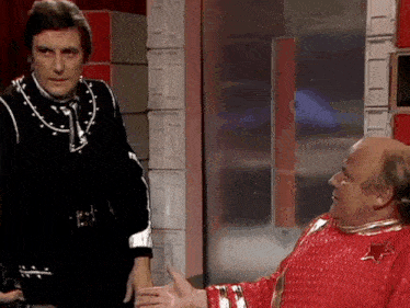 two men are standing next to each other and one of them is wearing a red costume with the letter v on it