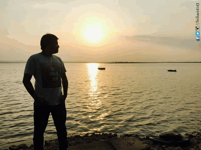 a man standing on the shore of a body of water with a sunset behind him