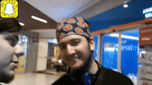 a man wearing a bandana and headphones smiles in front of a store that says ' snapchat '