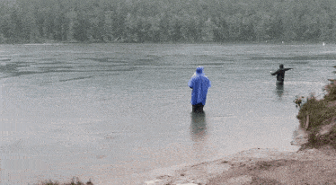 a man in a blue raincoat is standing in the water .