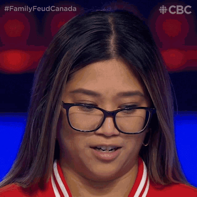 a close up of a woman wearing glasses and a red shirt with the words family feud canada behind her