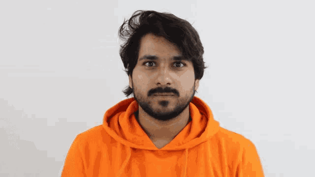 a man with a beard wearing an orange hoodie is making a funny face
