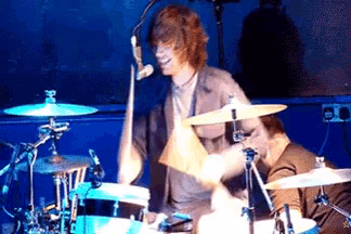 a man is playing drums in front of a microphone with the letter h on the cymbal
