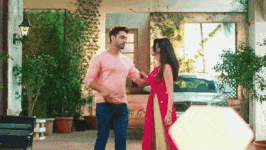 a man and a woman are standing in front of a house . the woman is wearing a red dress .