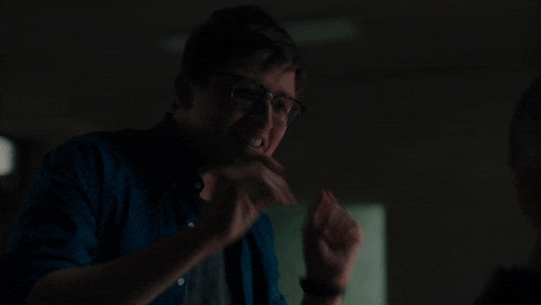 a man in a blue shirt and glasses is pointing at the camera .