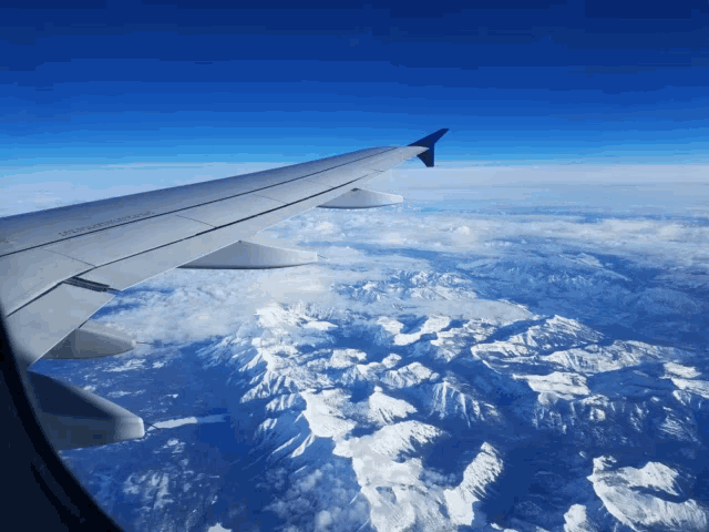 the wing of an airplane is visible above the clouds and mountains