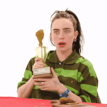 a woman in a green and brown striped shirt is holding a trophy that says winner " hot ones versus "