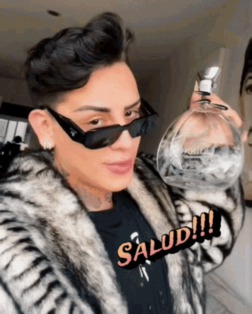 a man wearing sunglasses and a fur coat is holding a glass that says salud on it