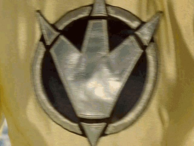 a close up of a yellow shirt with a silver symbol on it