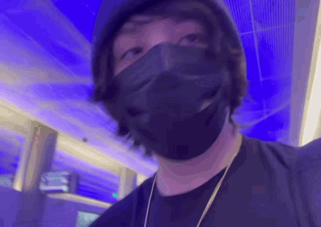 a man wearing a black mask and a hat is standing in front of a blue light .