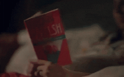 a person is laying on a bed reading a book .