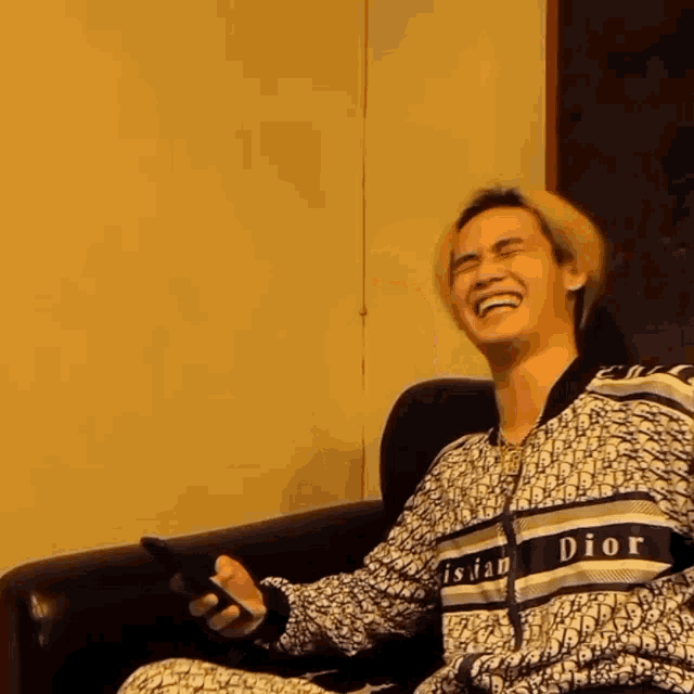 a man wearing a christian dior jacket is laughing and holding a cell phone