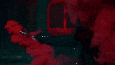 a person in a hood is standing in a room with red smoke coming out of it .