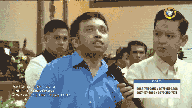 a man in a blue shirt is holding a microphone and looking up