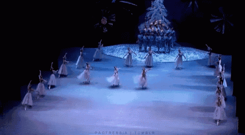 a group of ballet dancers are performing on a stage in front of a christmas tree .