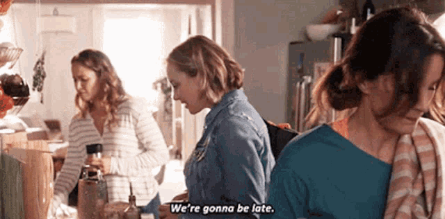 three women are standing in a kitchen and one of them is saying `` we 're gonna be late . ''