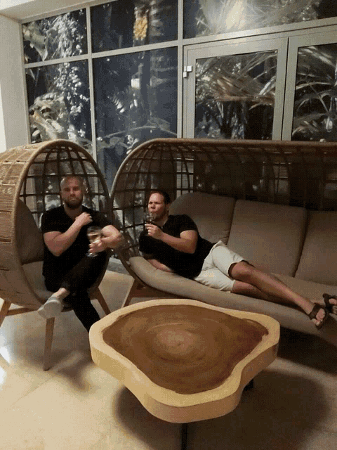 two men sitting on a couch with glasses of wine