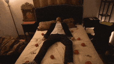 a man in a suit laying on a bed with apples around him